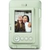 Mint-green Fujifilm instant camera displaying a selfie of two smiling women against a white brick wall