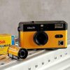 Vintage Ultra F9 camera with yellow leatherette body and black top, placed on a metal shelf beside film boxes and rolls.