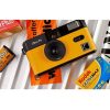 Yellow vintage camera resting on a striped surface with film boxes around it.