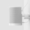 White wall-mounted speaker with perforated grille and external mounting bracket, connected by a cable to a wall socket.
