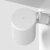 White cylindrical smart speaker mounted to a wall with a curved mounting bracket, facing outward.