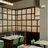 Cozy restaurant corner with a black-framed frosted glass wall, a black leather booth, and green chairs around white tables set with glasses and candles.