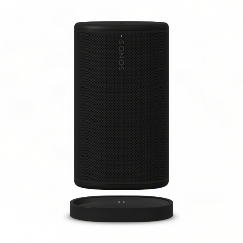 Black cylindrical Sonos wireless speaker with perforated grille, standing next to its round charging dock on a white background.