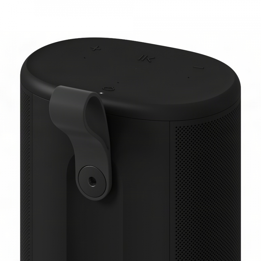 37128_10-900x900 | Kounio.gr Black cylindrical portable speaker with mesh sides and a fabric strap hinge on the side, top controls visible (volume and power).” ,