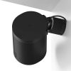 Black cylindrical wireless speaker mounted to a wall with a curved mounting arm, seen from above.