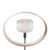 White wireless earbuds in their charging case centered inside a beige circular clock frame, connected by a cord at the bottom.