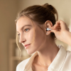 Woman placing white wireless earbud in her ear, wearing a light blouse in a softly lit room