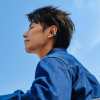 Side profile of a person wearing a wireless earbud in the right ear, against a clear blue sky.