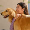 Young woman wearing a wireless earbud hugs a golden retriever outdoors.