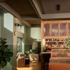 Cozy bar area with wooden bottle shelves, potted plants, and woven chairs beside a sunlit window.
