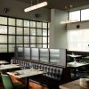 Restaurant dining area with black tufted leather booths, marble tables, and frosted glass dividers between tables.