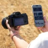 Person holding a DSLR camera in the left hand and a smartphone in the right hand outdoors on dry grass.