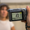 Close-up of a camera being held up to photograph a woman in a white shirt, with the subject blurred in the background.