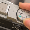 Close-up of a silver DSLR camera mode dial being turned by a finger, showing AUTO and P modes beside the hand.
