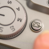 Close-up of a camera showing a large mode dial and a round button with a speech-bubble icon.