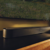 Silver Sonos soundbar resting on a dark TV stand beneath a wall-mounted screen with a nature wallpaper backdrop