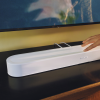 White Sonos soundbar lying on a black TV stand with a hand resting on its top edge.