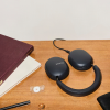 Sonos over-ear headphones on a wooden desk beside a maroon notebook and a pen.