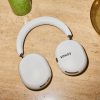 White Sonos over-ear wireless headphones laid on a light wooden countertop, showing the earcups and headband arc.