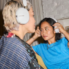 Two women wearing white Sonos over-ear headphones; one adjusts the other’s headphones indoors.