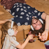 A man and a young girl on a brown couch wearing white over-ear headphones, playing with plastic dinosaur toys.