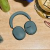 Teal Sonos over-ear headphones resting on a beige countertop with a hat and cash nearby