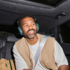 Man wearing teal over-ear headphones sits in the backseat of a car, secured with a seatbelt and smiling slightly.