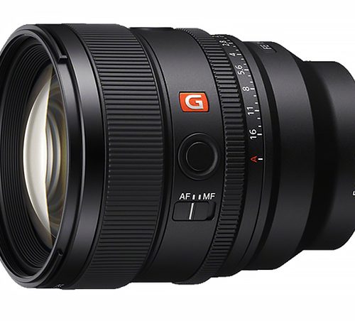 Close-up of a black interchangeable camera lens with an orange G badge, showing focus and zoom rings and an AF/MF switch.